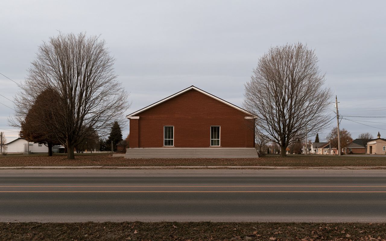 A single-storey red brick community hall set back from a village road, bare maples on either side.